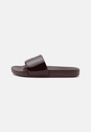 Σκούρο καφέ σανδάλι τύπου slip-on με φαρδιά γυαλιστερή λωρίδα και επίπεδη σόλα, εμφανιζόμενο από το πλάι σε ουδέτερο ανοιχτό φόντο.