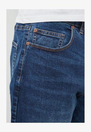 Mörkblå denimjeans har en klassisk design med kontrasterande sömmar, en ficka med lappar och kopparfärgad hårdvara på midjebandet.