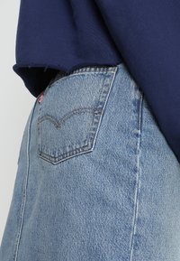 Ljusblå denimjeans med en distinkt bakficka och sömdekor, bärs med en marinblå skjorta med fransad nederkant.
