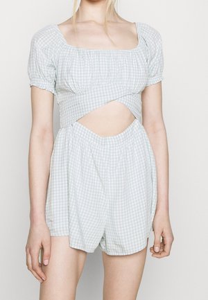 Vrouw draagt een lichtblauw geruit tweedelig outfit met pofmouwen, vierkante halslijn, uitgesneden taille en bijpassende hooggetailleerde shorts.