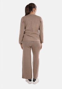 Maglione lavorato a maglia marrone e pantaloni a gamba larga coordinati, caratterizzati da una consistenza morbida, un design semplice e abbinati a sneaker bianche.