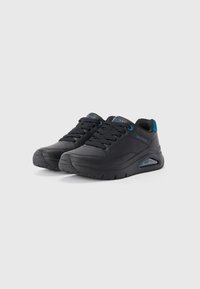 Baskets de sport noires avec une tige synthétique lisse, des accents texturés, un bout rond, des œillets bleus et un amorti d'air dans la semelle.