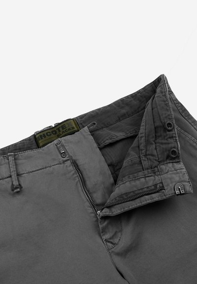 Pantaloni grigi con una texture solida, dotati di zip, chiusura a bottone e etichetta verde con marchio all'interno della vita.