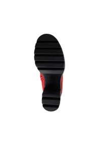 Suela roja de zapato con una superficie negra texturada; presenta ranuras anchas para tracción y una forma redondeada.