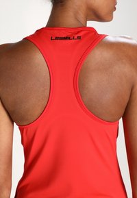 Rode sporttanktop met racerbackontwerp, gestructureerde stof en een zwart "LES MILLS"-logo op de achterkant van de halslijn.