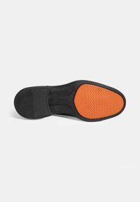 Zwarte schoenenzool van gestructureerd zwart rubber met een centrale oranje rubberen sectie met een geribbelde gripoppervlakte. Rond ontwerp van de hak.