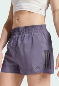 Lila Sportshorts mit einem elastischen Bund, die drei schwarze vertikale Streifen und ein Logo-Akzent auf der unteren linken Seite aufweisen.