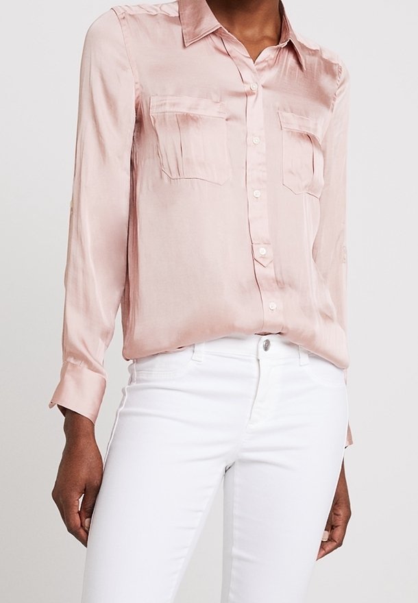 Ljusrosa satinblus med knappupptill, krage och två bröstfickor, i kombination med vita jeans. Långa ärmar med knappmanschetter.