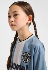 Ljusblå fotbollströja med vit randig design och mörka detaljer, med en rund logotyp på framsidan och en svart krage.