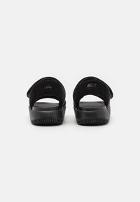Sandales noires Nike avec des sangles souples, des semelles texturées et une semelle plate, comportant un logo en relief sur le talon. Design minimaliste.