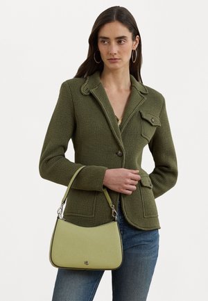 Kvinde iført en tekstureret olivengrøn blazer og jeans holder en lysegrøn håndtaske med kort rem og sølvhardware.