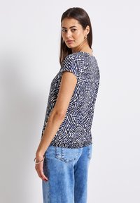 Camiseta de manga corta con un patrón geométrico en azul marino y crema, con un dobladillo ligeramente elástico y un corte holgado, combinada con jeans de color azul claro.