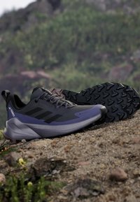 Tmavě šedé turistické boty s černými akcenty, texturovaná gumová podešev, polstrovaná mezipodešev a štítek GORE-TEX pro voděodolnost.