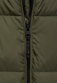 Olivgrüne Steppjacke mit einem schwarzen Reißverschluss. Verfügt über eine gesteppte Textur, horizontale Nähte und eine strapazierfähige Stoffoberfläche.