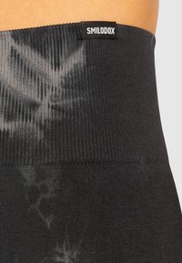 Leggings neri a vita alta con cintura a coste, caratterizzati da un motivo tie-dye su un tessuto liscio, con un piccolo etichetta del brand nella parte superiore.