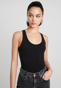 Bodysuit noir sans manches avec un décolleté arrondi, fabriqué en tissu lisse, associé à un jean noir délavé taille haute. Design minimaliste.