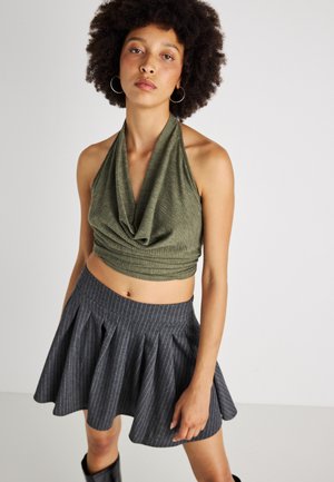 Olívovo zelený bezrukávový crop top s drapovaným výstrihom, skombinovaný so sivou pruhovanou plisovanou minisukňou. Hladká textúra látky, priliehavý strih.