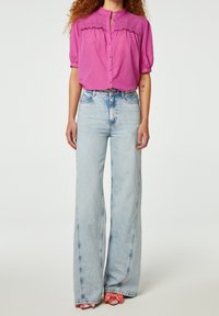 Lichtroze blouse met pofmouwen en geborduurde inzet, gecombineerd met hoge taille, blauwe wijde jeans. Glad materiaal en een ontspannen pasvorm.