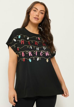 Femme aux longs cheveux bruns portant un t-shirt noir avec des lumières de fête colorées et les mots "Merry and Bright."