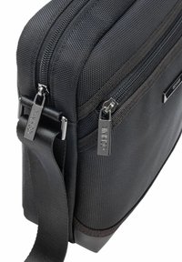 Czarna torba na ramię z teksturowanej tkaniny, podwójnymi zamykanymi kieszeniami i metalowymi detalami z akcentami marki. W zestawie regulowany pasek.