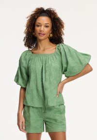 Top verde chiaro texturato con ampie maniche a sbuffo e scollo quadrato, abbinato a pantaloni corti coordinati, caratterizzati da un sottile motivo in rilievo.