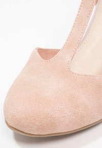 Chaussure en daim rose clair pour femme avec bout arrondi et strap sur le cou-de-pied, photographiée sur fond blanc.