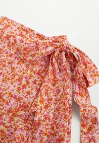 Bloemenriem in roze en oranje tinten, gemaakt van lichtgewicht stof. Bevat een strikdetail en een zachte, textuurvolle oppervlakte met een verspreide bloemenpatroon.