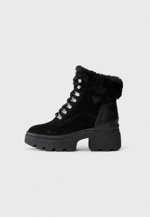 Botas de tornozelo em camurça preta com colarinho de pelo sintético, ilhós de metal e sola de borracha grossa. Detalhe de logótipo em relevo no calcanhar. Apresenta um design com atacadores.
