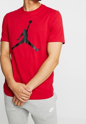 T-shirt en coton rouge avec un grand logo noir de Jordan sur le devant, associé à un pantalon de jogging gris avec un logo blanc de Nike.