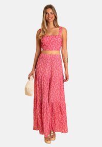 Vestido de dos piezas que cuenta con una parte superior corta de escote cuadrado y una falda larga con volantes. Hecho de tela rosa con un patrón de hojas y cintura fruncida.