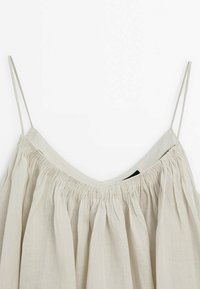 Haut sans manches beige clair avec fines bretelles spaghetti et tissu froncé le long de l'encolure.