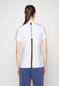 T-shirt blanc à manches courtes avec une rayure verticale noire et un logo au dos, fabriqué en tissu léger. Aucun motif ni embellissement.