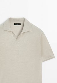 Polo beige à manches courtes avec col ouvert sans boutons, fabriqué en tissu maille léger.