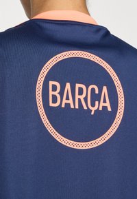 Navy blue sports jersey with an orange circular logo and the text "BARÇA" in the center. Smooth fabric with a crew neck design.