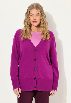 Živý purpurový kardigan, zapínání na pět černých knoflíků, žebrované manžety a lem, v kombinaci se světle růžovým topem pod ním.