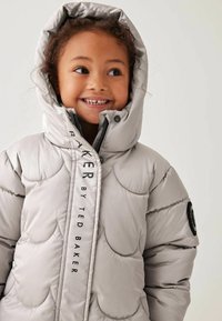 Lys grå pufferjakke med scallopet quiltet design, detaljering med sort logo og hætte; har elegante lynlåse og trykknapper.