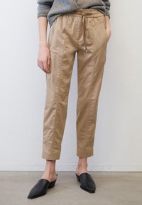 Beige tapering broeken met een trekkoord in de taille, voorzakken met rits en gestikte details. Gekleed met zwarte block-heeled muiltjes.