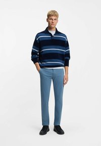 Pulovr s proužky v námořnické a světle modré barvě, s límečkem, doplněný o světle modré úzké kalhoty a černé tenisky.