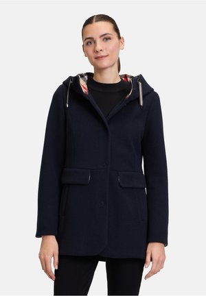 Navy wool blend coat with a hood, featuring a plaid lining, two front pockets, and silver hardware accents. Tailored shape with a button front.