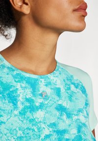Camiseta atlética turquesa com um padrão texturizado e abstrato. Apresenta um decote redondo e um pequeno logo na frente, com mangas curtas e estampadas.