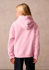 Felpa con cappuccio rosa dal tessuto morbido, caratterizzata da una vestibilità comoda, polsini a coste e un design del cappuccio senza cuciture. Abbinata a pantaloni cargo neri.
