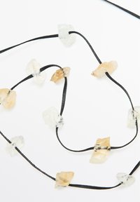 Collana in corda nera con pietre naturali traslucide e opache di forma irregolare nelle tonalità di chiaro e beige.