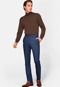 Ciemnobrązowy sweter z golfem w połączeniu z dopasowanymi, niebieskimi spodniami w kratę i brązowymi skórzanymi butami; dopasowany krój o gładkiej fakturze.