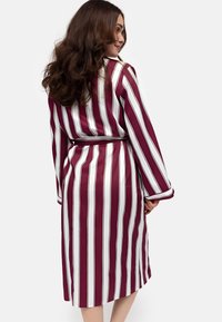 Bata de rayas burdeos y blanca con cinturón en la cintura y mangas largas. Textura sedosa con rayas verticales en contraste y puños doblados.