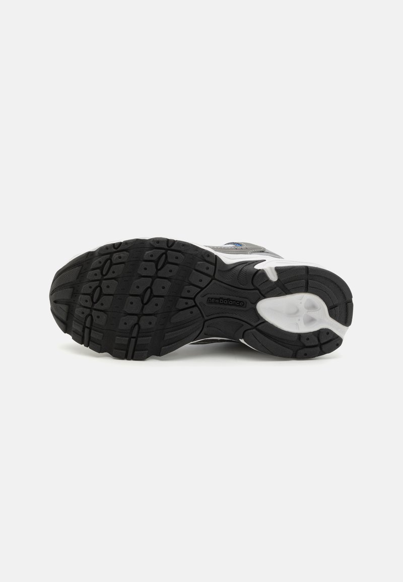 Suela de zapato de goma negra con un patrón de textura, que presenta acentos blancos y un recubrimiento gris. Incluye un logo en la suela.
