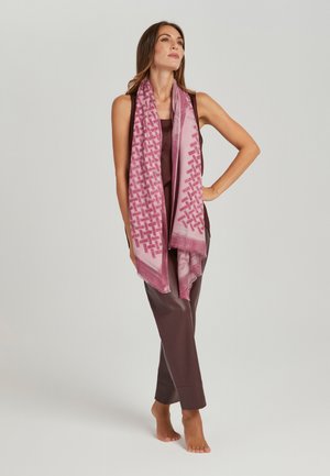 Geweven sjaal in gradient roze met geometrische patronen, gedrapeerd over een model dat een donkerbruin outfit draagt. Zachte textuur en franjes aan de randen.