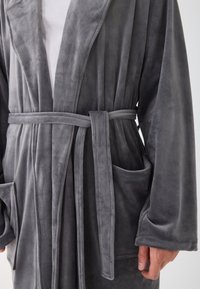 Sivi flis bathrobe s dugim rukavima, vezanom remenom i s dva prednja džepa. Mekana tekstura s glatkom završnom obradom i suptilnim sjajem.