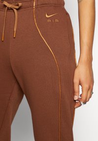 Ruske Nike hlače za trčanje z žametenim materialom, zlatim akcentnim pasom in logotipom. Imajo nastavljiv pas z vrvico in stranske žepe.