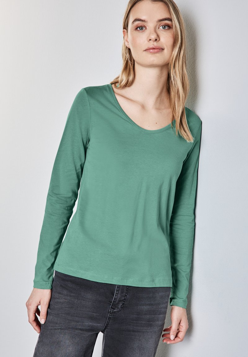 Grünes Langarmshirt aus einem sanften, glatten Stoff mit Rundhalsausschnitt und slim fit, kombiniert mit dunklen Jeans.