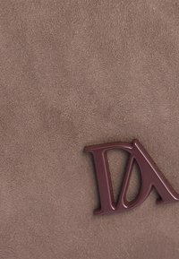 Material de ante marrón con una textura suave, con un destacado logo marrón "DA" hecho de plástico brillante.